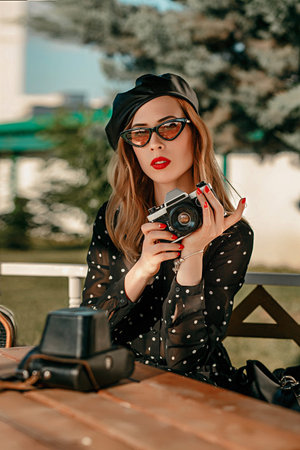 Young woman in a vintage black polka-dot dress with an old camera in her hands posing on the street