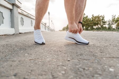 Caucasian guy in a blue t-shirt and black shorts, who ties his laces on white sports shoes before Joggingの写真素材