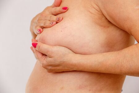 60 year old older woman checks her big Breasts for cancer on a light isolatedの写真素材