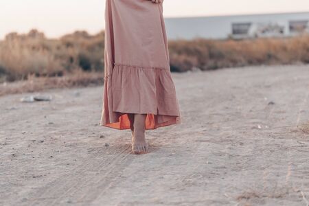 feet of a woman in a pink dress walking on the sand during sunsetの写真素材