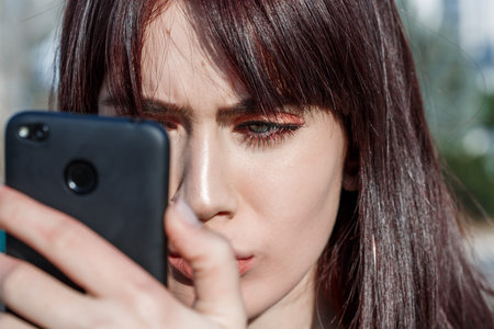 beautiful young Caucasian brown haired girl puts Foundation on her face using the phone as a mirror