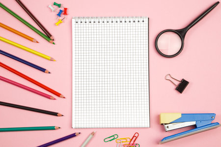 colored pencils, stationery, paper notebook with pen and magnifier on pink isolated background. top...