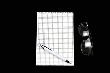 paper notebook with ballpoint pen and optical glasses on black isolated backgroundの写真素材