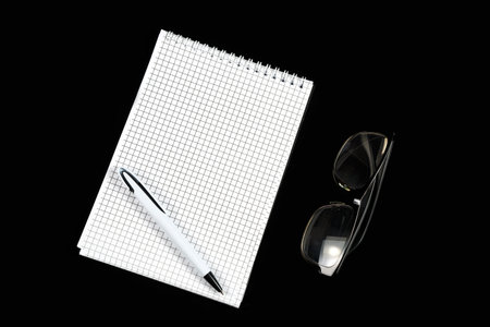 paper notebook with ballpoint pen and optical glasses on black isolated background