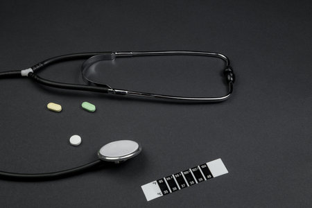 medical stethoscope, medication and thermometer-strip on black isolated background