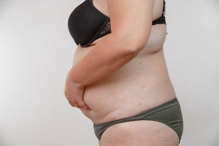 woman squeezes her stomach, girl squeezes fat on her stomach, fatty folds on the abdomen. concept for medicine and cosmetologyの写真素材