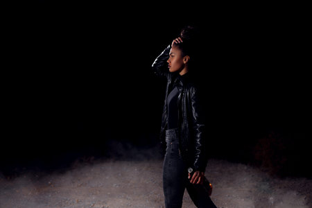 a young African-American mulatto girl in a leather jacket and black clothes is walking along an...