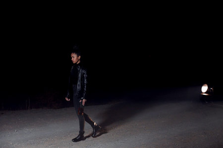 a young African-American mulatto girl in a leather jacket and black clothes is walking along an...
