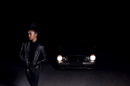 a young African American mulatto girl in a leather jacket and black clothes poses on an abandoned...
