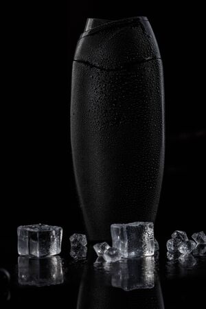 black sweaty plastic bottle for shampoo or shower gel on a black isolated background. there are also ice cubes in the backgroundの写真素材