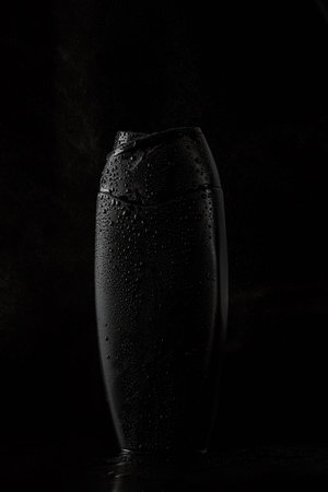 black sweaty plastic bottle for shampoo or shower gel on black isolated background
