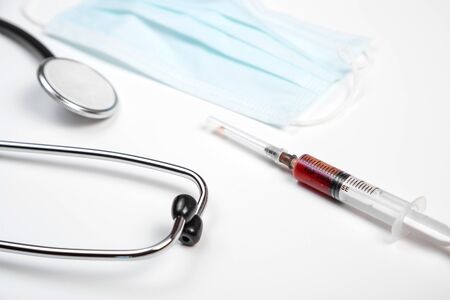 medical stethoscope, disposable mask and syringe with blood samples on a white isolated backgroundの写真素材