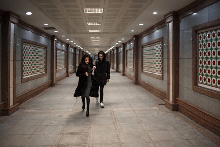 a young beautiful woman tries to escape from a robber in black clothes . in the underpass. at nightの写真素材