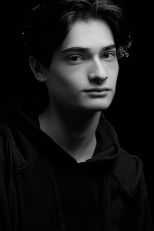 dramatic portrait of a young guy in a black hoodie on a black background. black and white photoの写真素材