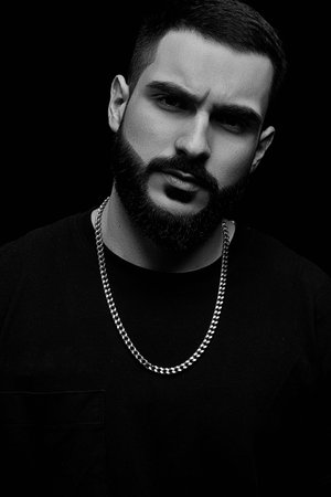 close-up of a dramatic portrait of a young serious guy, musician, singer, rapper with a beard in...