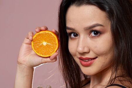 young beautiful slender Asian girl in a swimsuit . holding an orange. smiles. on a pink isolated background.の写真素材