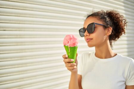 a young beautiful African-American girl in a white t-shirt and light jeans eats ice cream on a Sunny day. selective focusing. small focus area.の写真素材