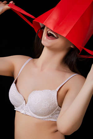 a young beautiful woman in white underwear with a red paper shopping bag poses and smiles. on a black isolated background.の写真素材