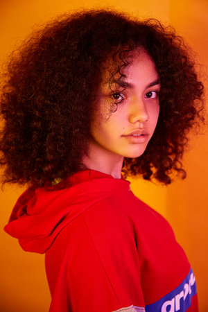 a young beautiful African-American girl in a red hoodie on a yellow isolated background in yellow...