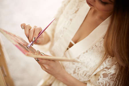 a young beautiful Asian woman in a beige lace robe put on morning makeup and uses eye shadow, blush and Foundation. in the bedroom. shallow depth of focus. selective focus.の写真素材