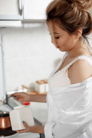 young beautiful Asian girl in beige lace shorts, white shirt drinking coffee standing on the balcony. selective focus. small focus area.の写真素材
