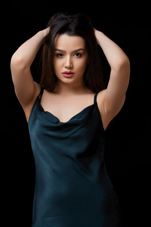 young woman in dark blue dress dress. on a black isolated background.she touches her face with her hand, touches her hair.の写真素材
