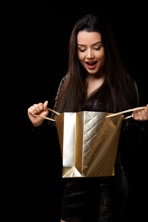 a young woman in a black dress is happy to receive a gift in a gold-colored package.の写真素材