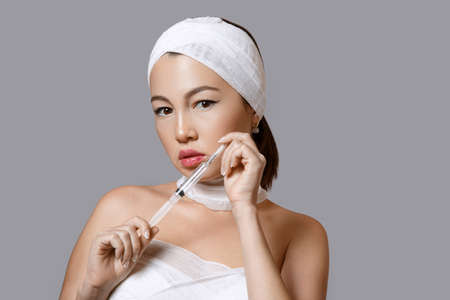 fashion portrait of a young beautiful Asian woman on an isolated background with a syringe in her hands. the syringe contains injections of drugs for cosmetology.の写真素材