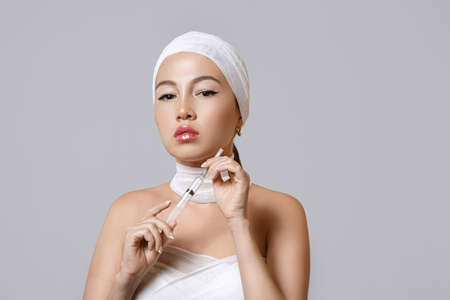fashion portrait of a young beautiful Asian woman on an isolated background with a syringe in her hands. the syringe contains injections of drugs for cosmetology.の写真素材