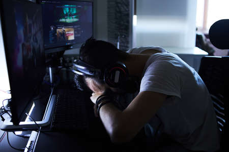 a young 30-year-old gamer is sitting at a computer, playing computer games, nervous, angry, worried.selective focus with low depth of focus.の写真素材
