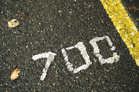 Number seven hundred on a wet asphalt road. Distance indication number.