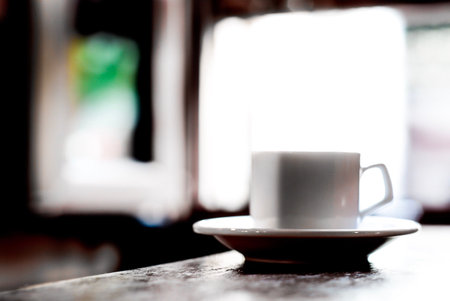 A cup of coffee on a wood table with an open window on the background.