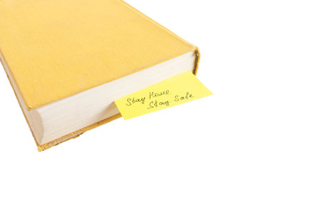 Yellow old book with âStay Home, Stay Safeâ message isolated on white. Home isolation and education concept.の写真素材