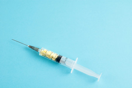 A medical syringe with yellow pills inside on blue background