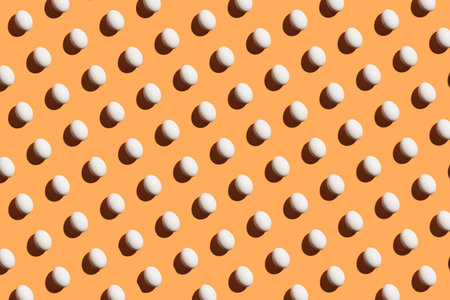 Minimal pattern made of white eggs under bright light with dark shadows on orange background