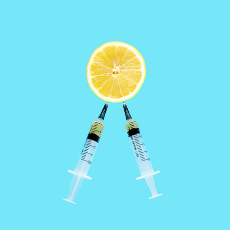 Minimal concept with two syringes suching out lemon juice isolaten on blue backgroundの写真素材