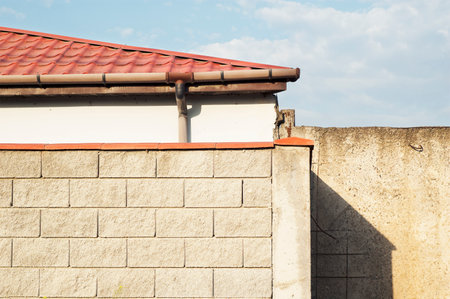 Part of a house with red rood and a wall fence with hard shadow.の写真素材