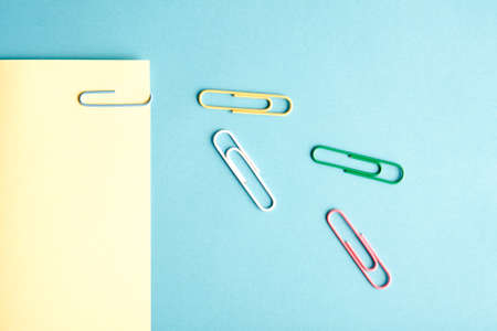 Colorful paper clips on bright blue and yellow background. Minimalist concept flat lay.の写真素材