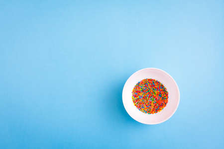 White pbowl with colorful sugar sprinkles on blue background with free copy paste space.の写真素材