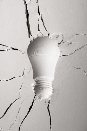 Light bulb shaped imprint on white granular background with cracks.