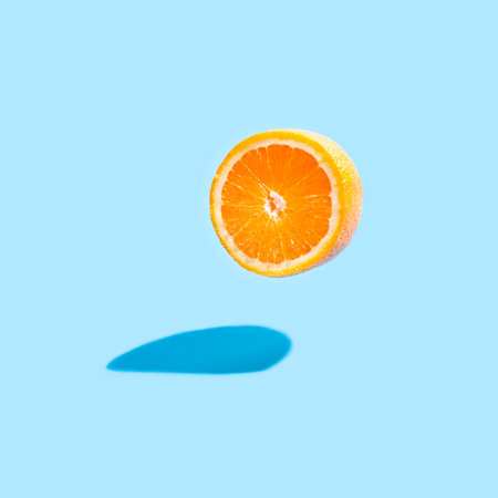 Isolated orange half with a real shadow on blue background. Flying orange on blue.の写真素材