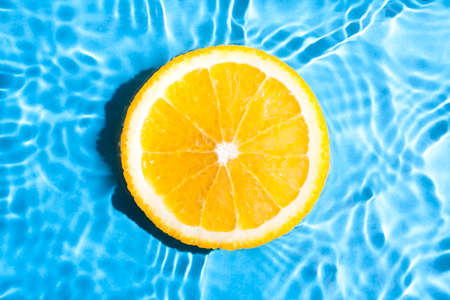 Slice of fresh orange in water on blue abstract background. Orange slice on blurry blue abstract background.の写真素材