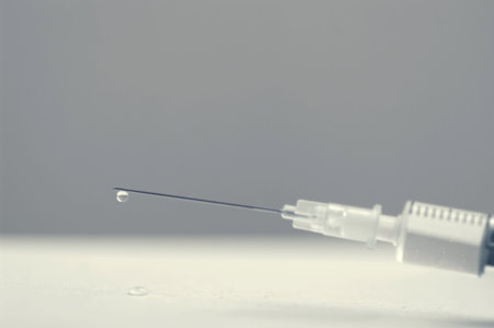 Close up monochrome image of a siringe with droplet on needle