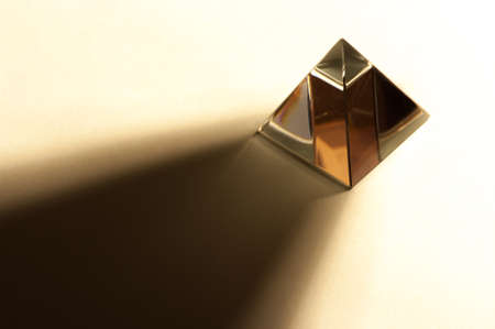 Minimalist still life image of a shiny pyramid in warm color tone. Pyramid throwing hard shadow.の写真素材