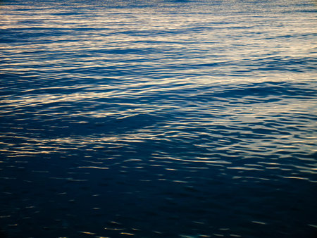 Dark blue sea water surface with dim sunlight reflections.