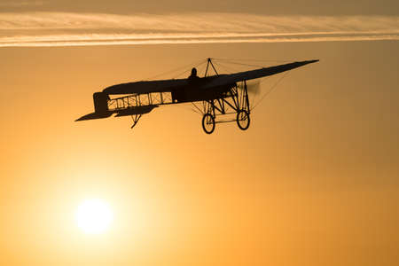 Old vintage plane flying in an orange sky at sunsetの写真素材