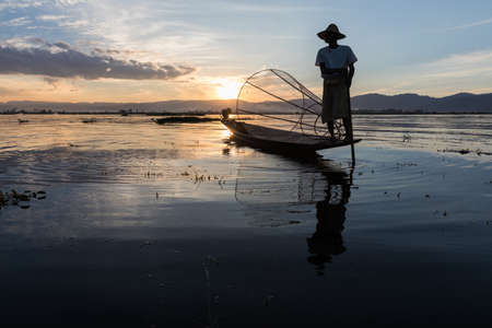 Fishermen fishing with big net in traditional and unique one-leg rowing style during sunset on Inle Lake in Shan State, Myanmar, Burmaの写真素材