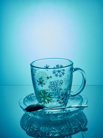 Empty mug on a saucer with a mirror reflection.In the saucer lies a spoon.The mug stands on a blue...