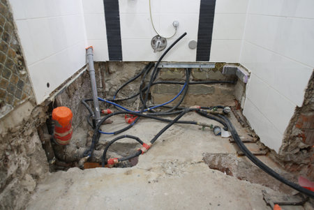 The plumbing work is currently in progress, showcasing exposed pipes and a bare floor in a bathroom renovation projectの写真素材