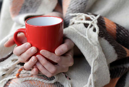 red mug in his hands and a warm blanket for restの写真素材